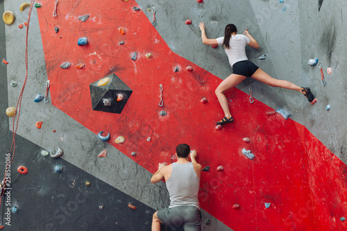 Sporty man and woman having competition at rock climbing gym. Low angle view.