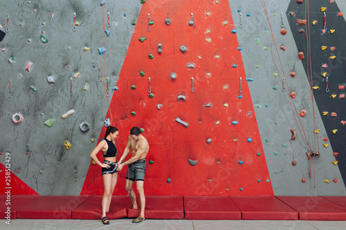 sport climbing protection, personla trainer takes care of a yung begginer climber. copy space. full length photo