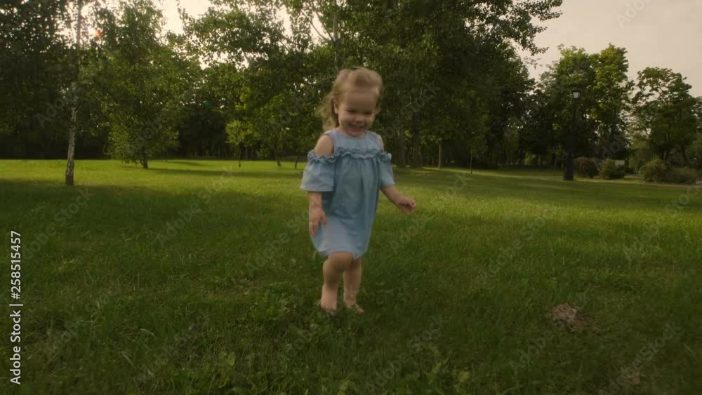 Baby girl running through the grass and rushes into mother hands in garden in sunset sunlight. Slow motion. Happy smiling baby girl. Baby girl running through the grass and rushes into mother hands in garden in sunset sunlight. Slow motion. Happy smiling baby girl.
