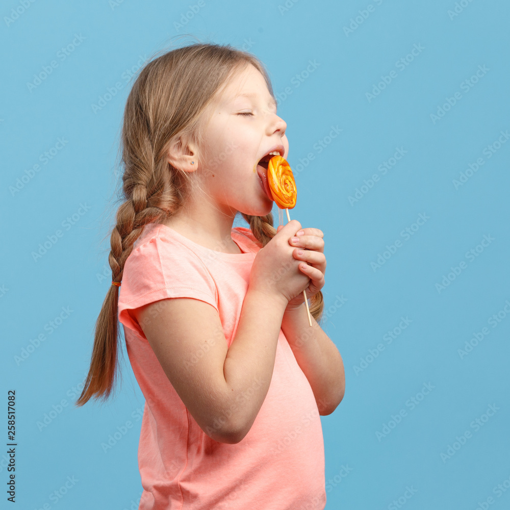 Cute little girl eats ice cream and laughs in studio over blue background Cute little girl eats ice cream and laughs in studio over blue background