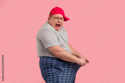 Overweight man pulling ahead his pants, looking at camera while screaming, being shocked or extremely upset with that he has seen in pants. Lost weight concept. Can not lose weight photo