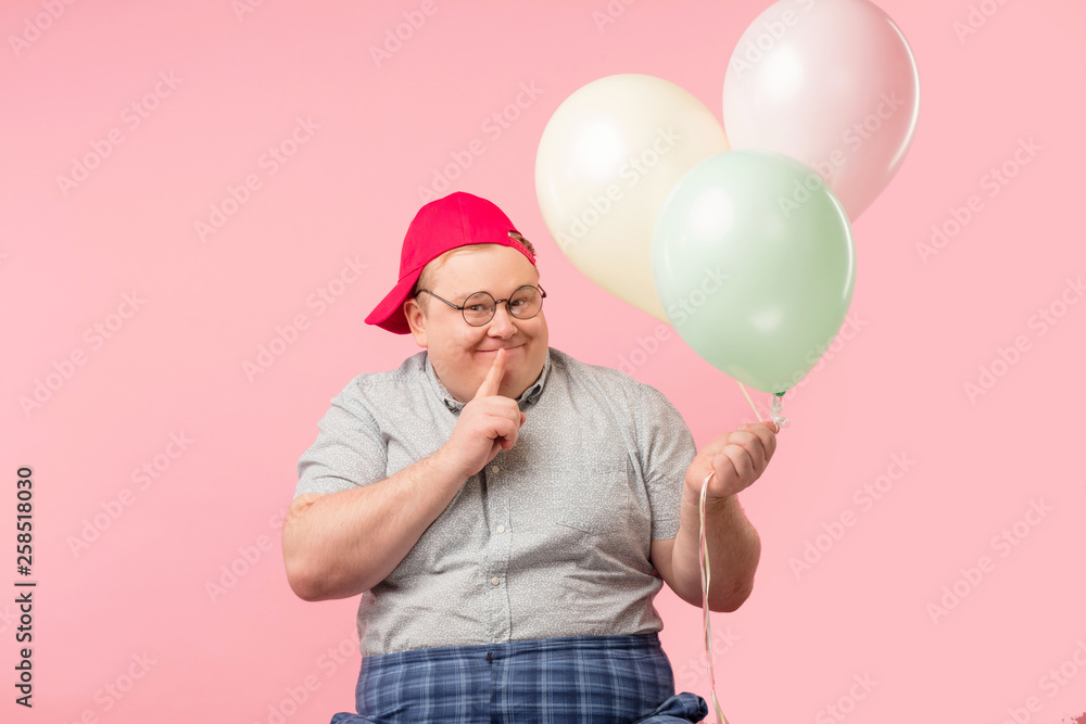 Portrait of funny plump middle-aged male animator holds finger near mouth, looks misteriously, asks to keep secret from children that he has brought the air balloons. Children, Celebration, Animation Portrait of funny plump middle-aged male animator holds finger near mouth, looks misteriously, asks to keep secret from children that he has brought the air balloons. Children, Celebration, Animation