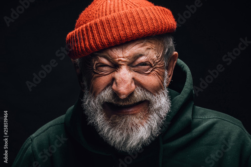 Grey- haired aged grandfather feeling overjoyed and excited while telling about his trip to mountains. Old man dressed in red knitted hat and green hoodie. Happy to be active in retirement