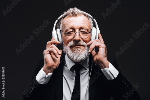 Studio isolated shot of handsome mature grey-haired businessman with headphones, listening songs loudly, relaxing and having a rest for his soul. People, leisure and modern technology concept.