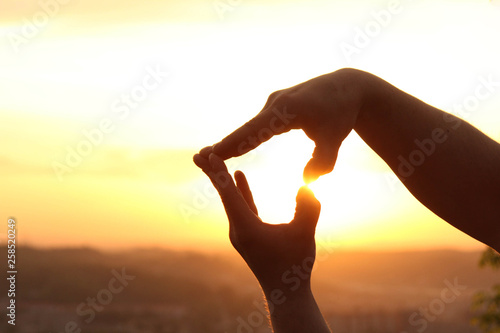 Hands make up a heart shape at sunset.