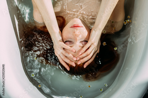 Young pretty redhead woman with coopery hair taking bath . Sensual sexy female model relaxing in a bathtub, close up. Youth and Skin and Body Care Concept. photo