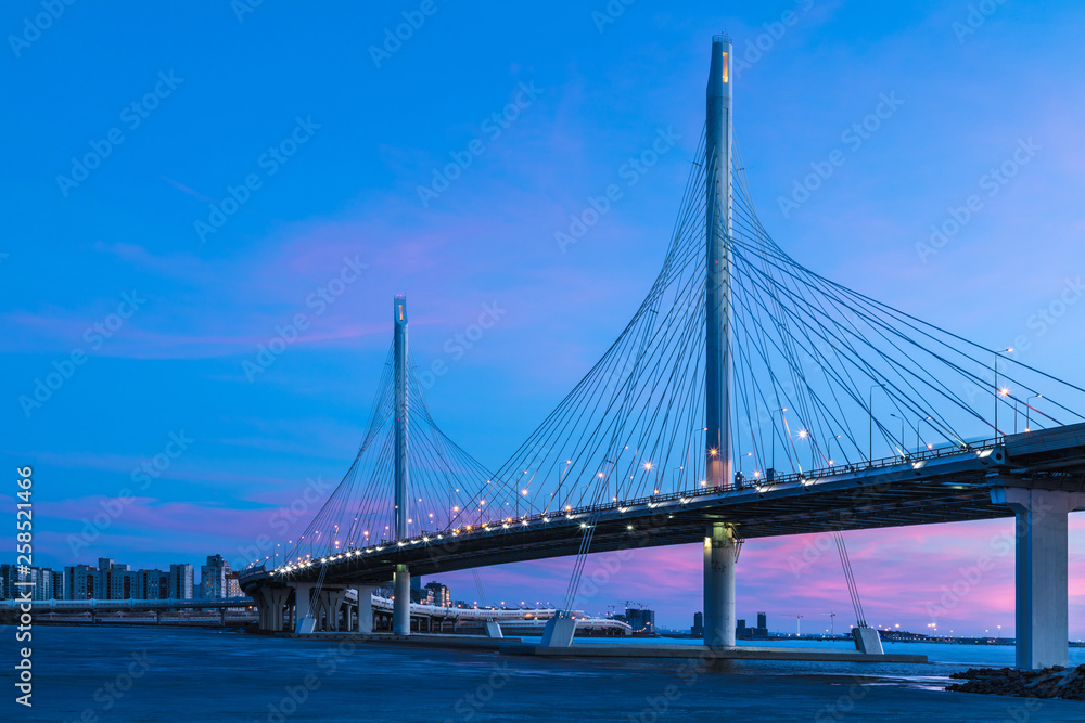 The bridge of circle highway road over Neva river near the mouth of it in the blue hour after the sunset. Night view on the buildings of Petersburg city and the Finish gulf