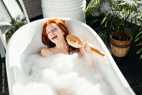 Vivacious emotional young woman with red hair bun taking bath at home, being in Poster Mural XXL