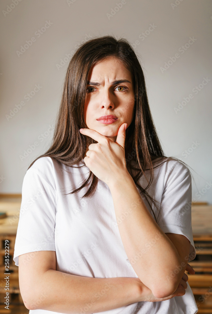Portrait of brunette longhaired woman wearing white t-shirt thinking about something with serious emotion Portrait of brunette longhaired woman wearing white t-shirt thinking about something with serious emotion