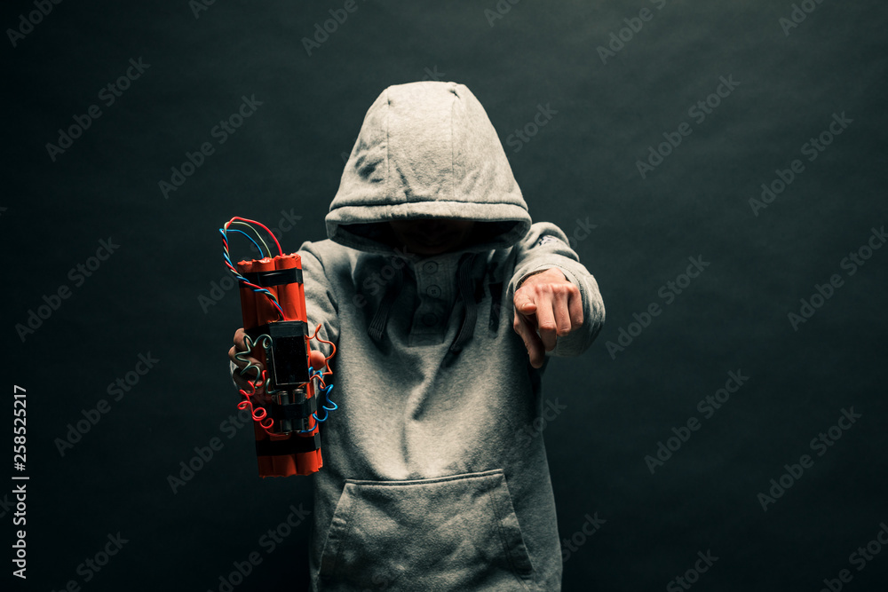 Φωτογραφία The silhouette of a man in the hood on a black background, his face is not visible, shows hands gesture and a time bomb