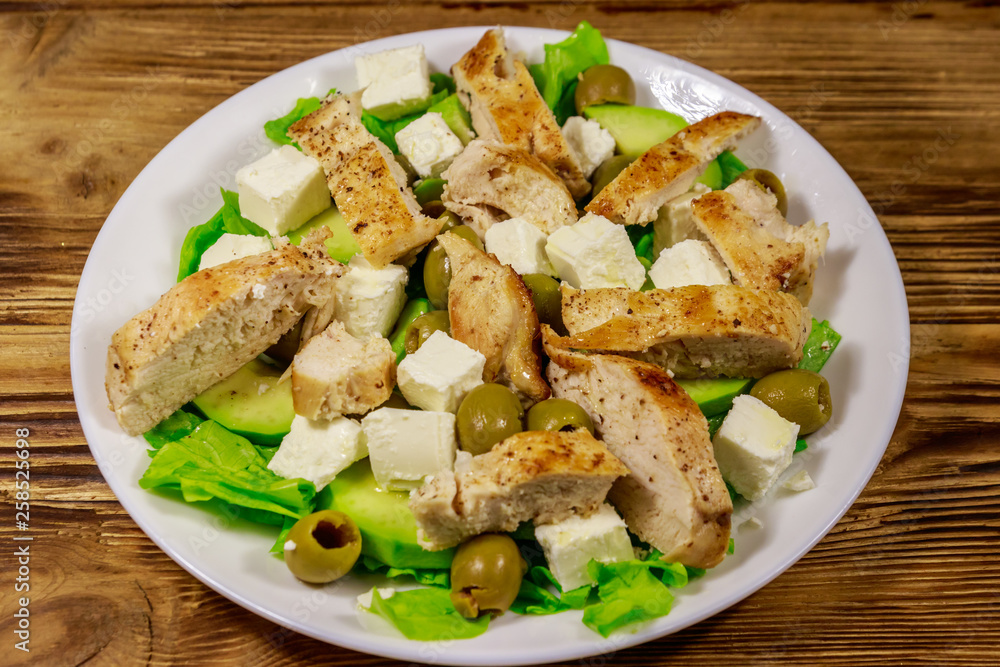 Tasty salad with fried chicken breast, green olives, feta cheese, avocado, lettuce and olive oil on wooden table Tasty salad with fried chicken breast, green olives, feta cheese, avocado, lettuce and olive oil on wooden table