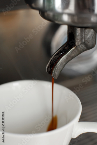 Close-up of freshly brewed coffee is poured from a coffee machine into a white cup