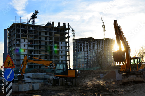 Two backhoe loaders during excavation work on the construction site of high residential buildings and offices. Sunset at a construction site © MaxSafaniuk