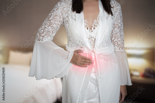 The woman in white silk nightgown and lace robe with stomach ache on the bedroom, inflammatory bowel disease, Lady in luxury white long nightwear having diarrhea at night, Irritable Bowel Syndrome photo