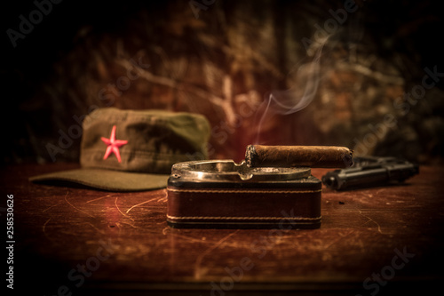 Close up of a Cuban cigar and ashtray on the wooden table. Communist dictator commander table in dark room. Army general`s work table concept.