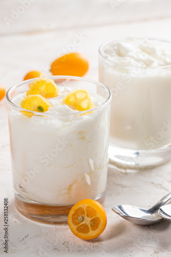 Two glasses with homemade fat yogurt with juicy kumquat  slices and two metal spoons on white background.