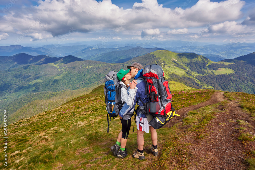 Man and woman standing and hugging on the top of the mountain, summer hike with backpacks