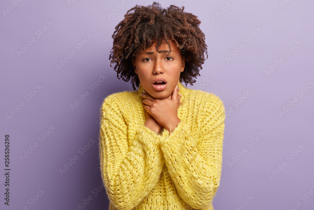 Asphyxiate and health problems concept. Desperate dark skinned woman has painful strangle in throat, suffers from suffocation, wears yellow jumper, demonstrates suicide gesture, isolated on purple Asphyxiate and health problems concept. Desperate dark skinned woman has painful strangle in throat, suffers from suffocation, wears yellow jumper, demonstrates suicide gesture, isolated on purple