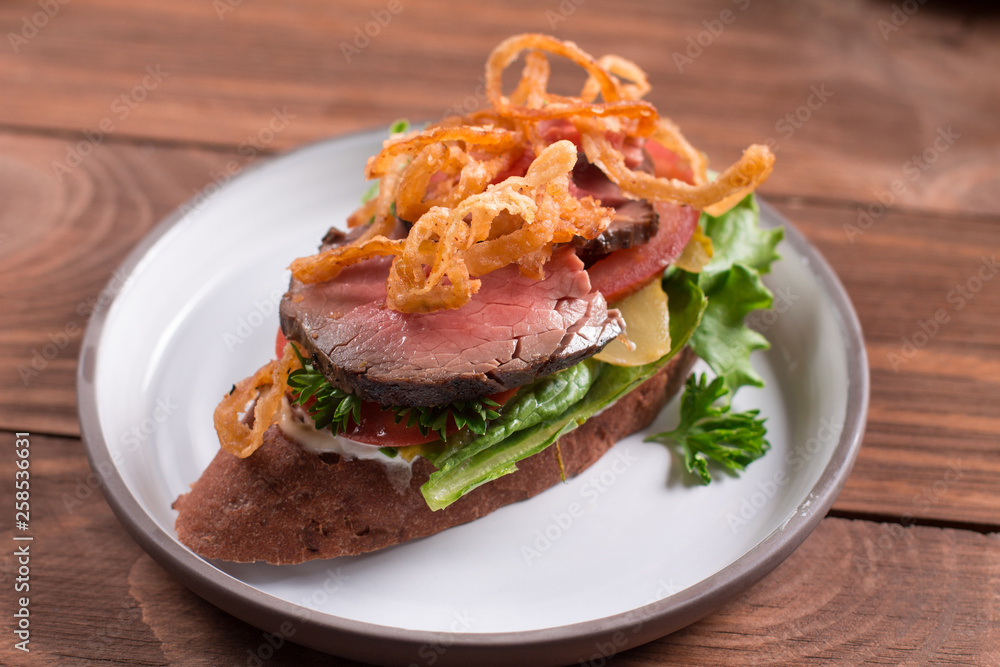 Grilled rye bread sandwich, corned beef, Swiss cheese, sauerkraut, fried onions and herbs. Wooden background Grilled rye bread sandwich, corned beef, Swiss cheese, sauerkraut, fried onions and herbs. Wooden background