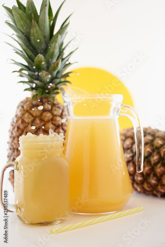 Jug and glass of pineapple juice with fruits on white background. Splash yellow drink. 