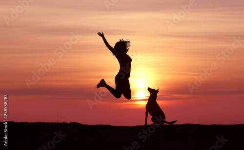 Girl and dog at sunset, Belgian Shepherd Malinois breed, incredible sunset, athletic girl jumping, the dog looks at the jumping girl