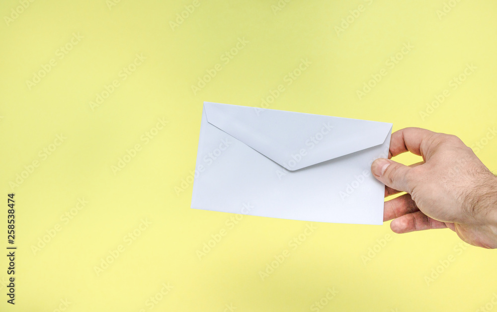 A hand is holding a white envelope on a yellow background. A hand is holding a white envelope on a yellow background.