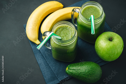 Green, healthy, detox smoothie from avocado, banana, apple in mason jar on blue napkin, dark background, vegetarian food