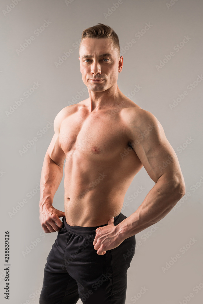 handsome male athlete with pumped muscles on gray background