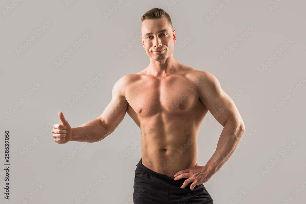 handsome male athlete with muscled muscles on gray background with hand gesture