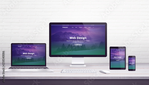 Web design studio concept with flat design responsive web site on display devices. Office work desk with brick wall in background.