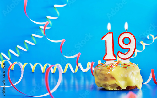 Birthday of nineteen years. Cupcake with white burning candle in the form of number 19. Vivid blue background with copy space