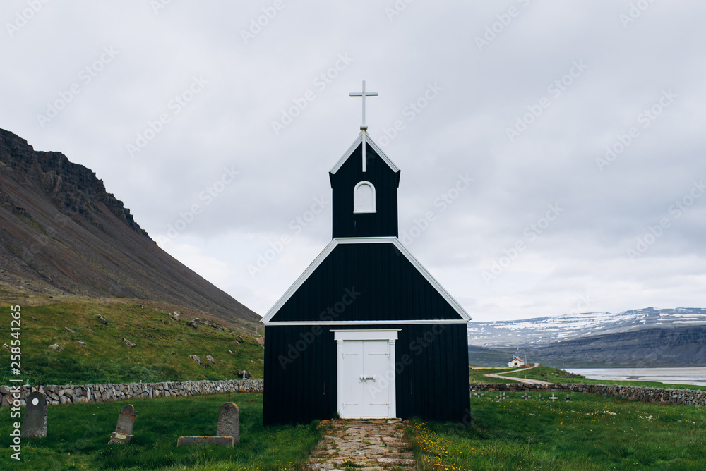 Black wooden church in the middle of the field. The church in Iceland stands on the background of the mountains.