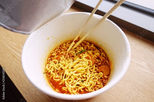 Top view of ramen cup or instant noodle cup with a fork, near a window in a warm light of morning, Korean noodle style,