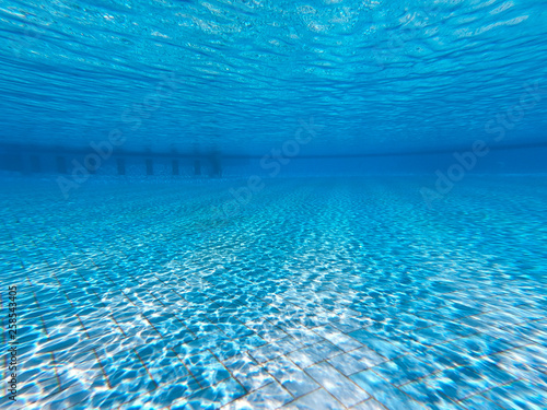Transparent clear water in the pool. Underwater photo of the regulatory pool. Blue water pool bottom background. Summer theme.