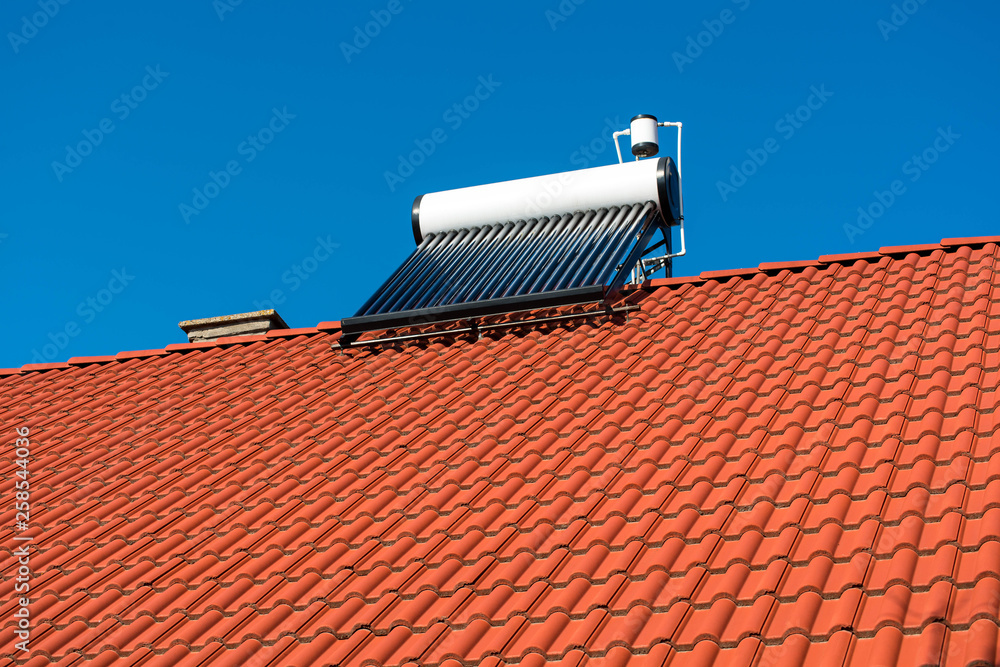 Solar water heater boiler on residentual house rooftop, perfect blue sky background.