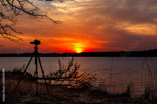 Silhouette of a camera taking pictures of a sunset on a lake.