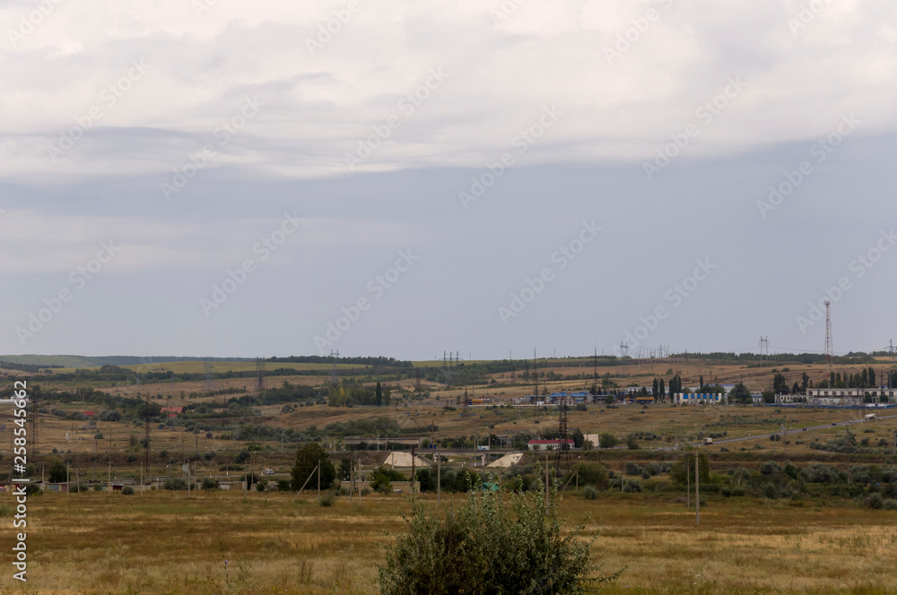 Gold meadow with lonely green trees far away and blue calm tender sky above. Yellow dry grass. Electric poles in the field. Small town far away.Travelling. Ural landscapes Gold meadow with lonely green trees far away and blue calm tender sky above. Yellow dry grass. Electric poles in the field. Small town far away.Travelling. Ural landscapes