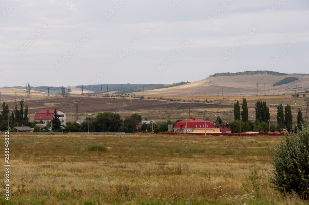 Gold meadow with lonely green trees far away and blue calm tender sky above. Yellow dry grass. Electric poles in the field. Small town far away.Travelling. Ural landscapes Gold meadow with lonely green trees far away and blue calm tender sky above. Yellow dry grass. Electric poles in the field. Small town far away.Travelling. Ural landscapes