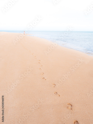 Footprints on a tropical beach, fading towards horizon, with a woman far away