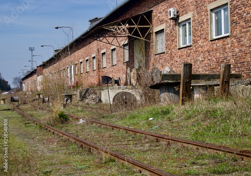 Abandoned, old, rusted railroad in high grass next to made of red brick store