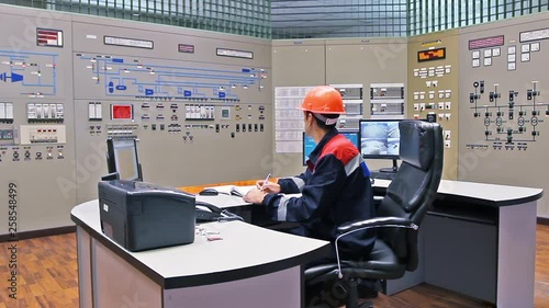 engineer sits at table in front of main control panel for gas compressor station and writes registry photo