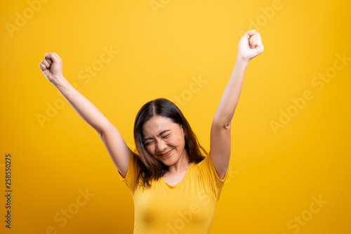 Happy woman make winning gesture isolated over yellow background photo