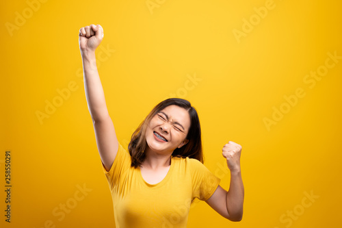 Happy woman make winning gesture isolated over yellow background