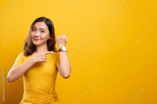 Happy woman holding hand with wrist watch isolated on a yellow background