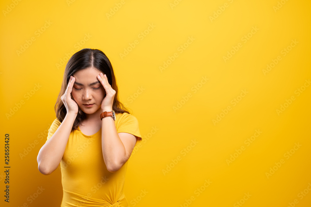 Woman has headache isolated over yellow background Woman has headache isolated over yellow background