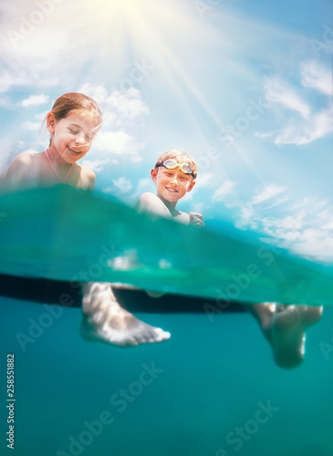 Sister and brother sitting on inflatable mattress and enjoying the sea water, cheerfully laughing when swim in the sea. Careless childhood time unusually unerwater camera shot image. photo