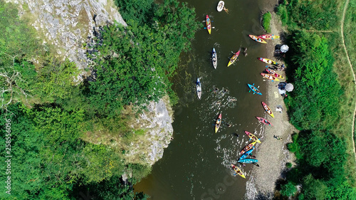 Aerial top view of people jumping into the water from high rock cliff and group of kayakers paddling down. Green scenery  rocky canyon landscape. View of kayaking and swimming in Belgium Europe