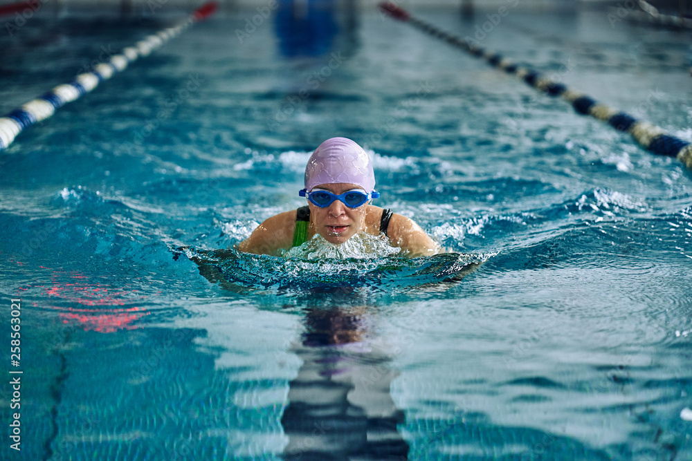 Female athlete swims with a butterfly style. Splashes of water scatter in different directions.