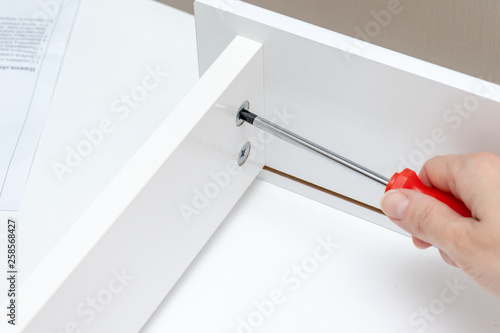 Hand assembling, tighting details of white furniture using a screwdriver