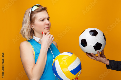 Athletic woman chooses between volleyball and soccer ball in studio.